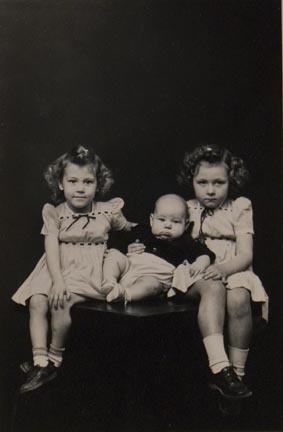 Untitled (twin girls with baby, seated on table)