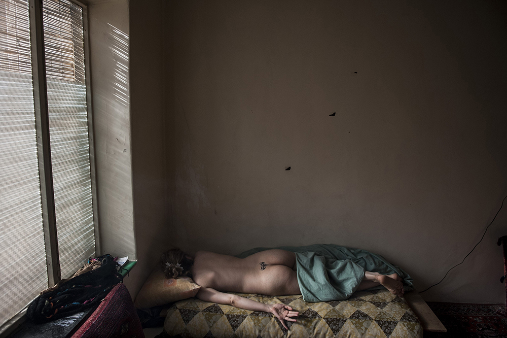 Tehran, Iran. A naked woman, with a tattoo at the base of her spine, lies on a bed. The woman is a prostitute working to pay for the cost of raising her two children.