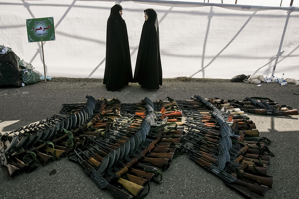 Tehran, Iran. Female members of the Basij, a voluntary militia, stand next to a pile of AK-47s following a military parade held to mark Basij Week.