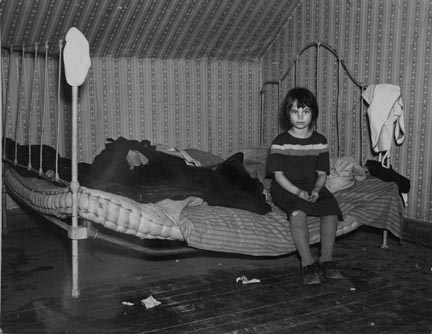 One of Edgar Allen's children sitting on the bed in the house on his farm. There are no sheets, pillowcases, or pillows (other than makeshift) in use. Bedding usually consists of castoff rags and a few old blankets. Near Milford, Iowa. They are helped by the Resettlement Administration