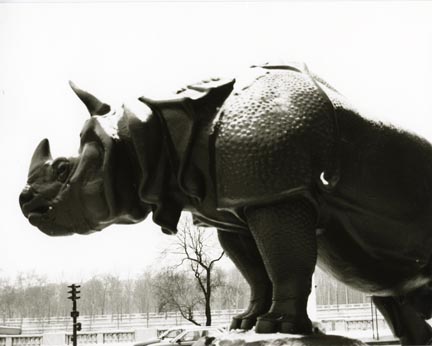 A statue of a rhinoceros.  Trees and telephone wires are in the background.
